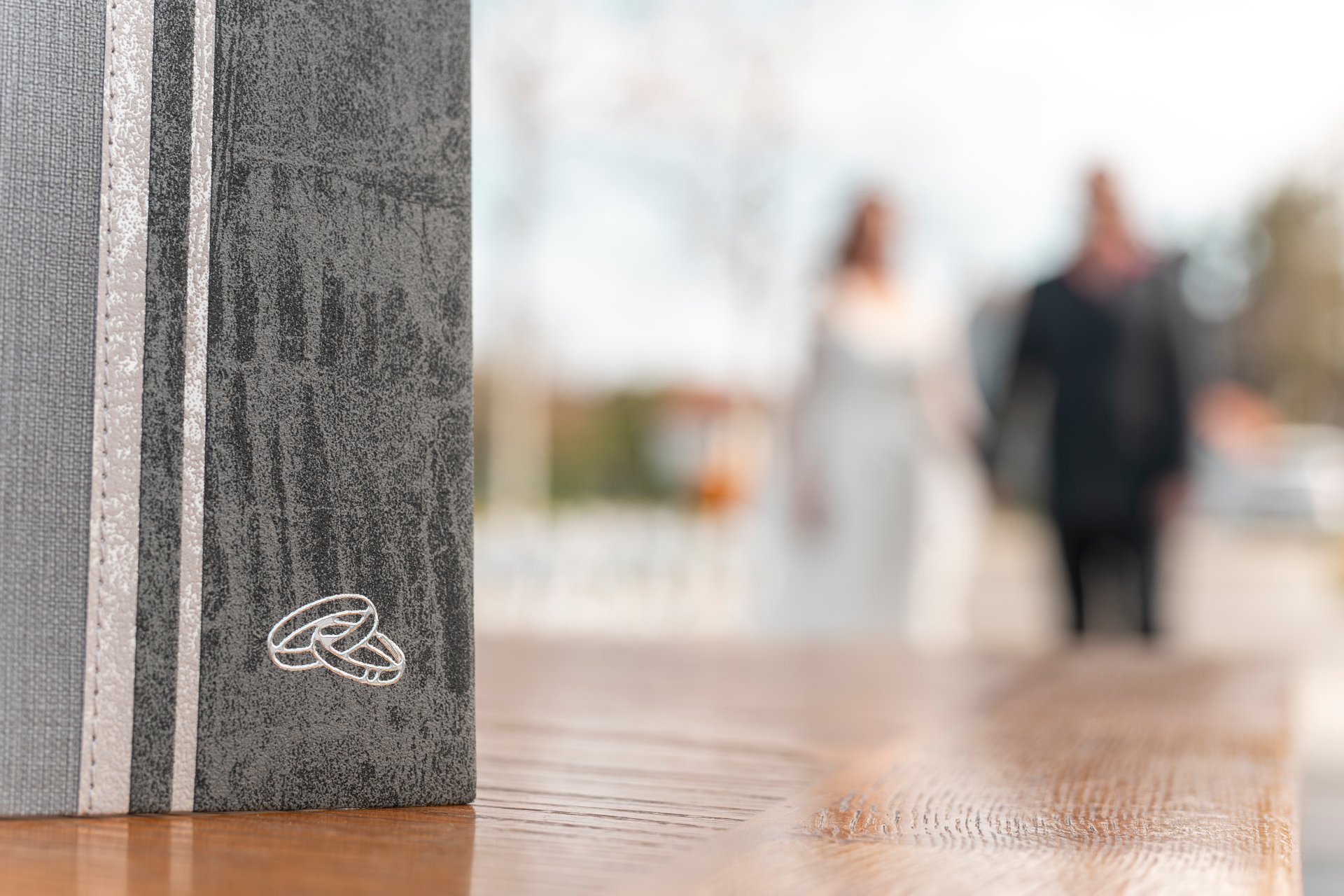 Grey family register with two wedding rings. A married couple in the blurred background.