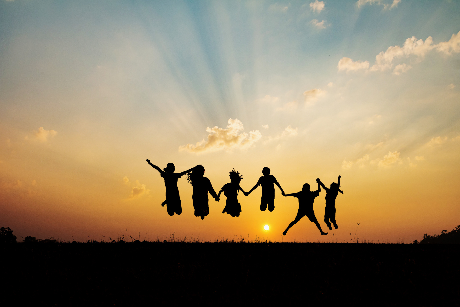 Silhouette einer Gruppe fröhlicher Kinder, die bei Sonnenuntergang im Sommer auf einem Berg spielen und herumspringen.