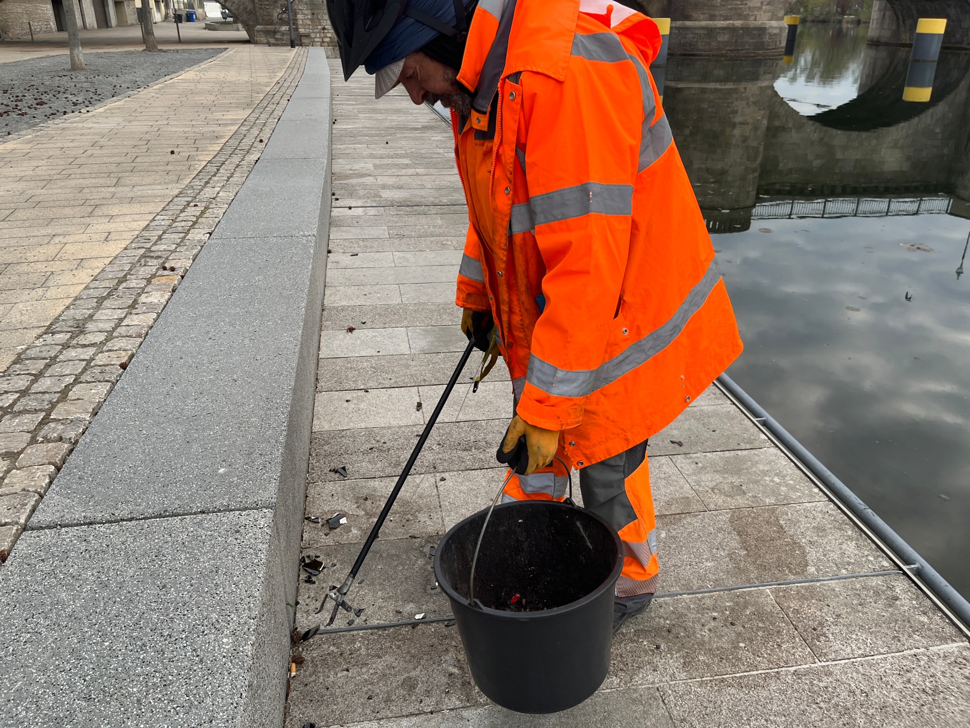 Stadtreiniger sammelt Müll am Mainkai vom Boden auf.