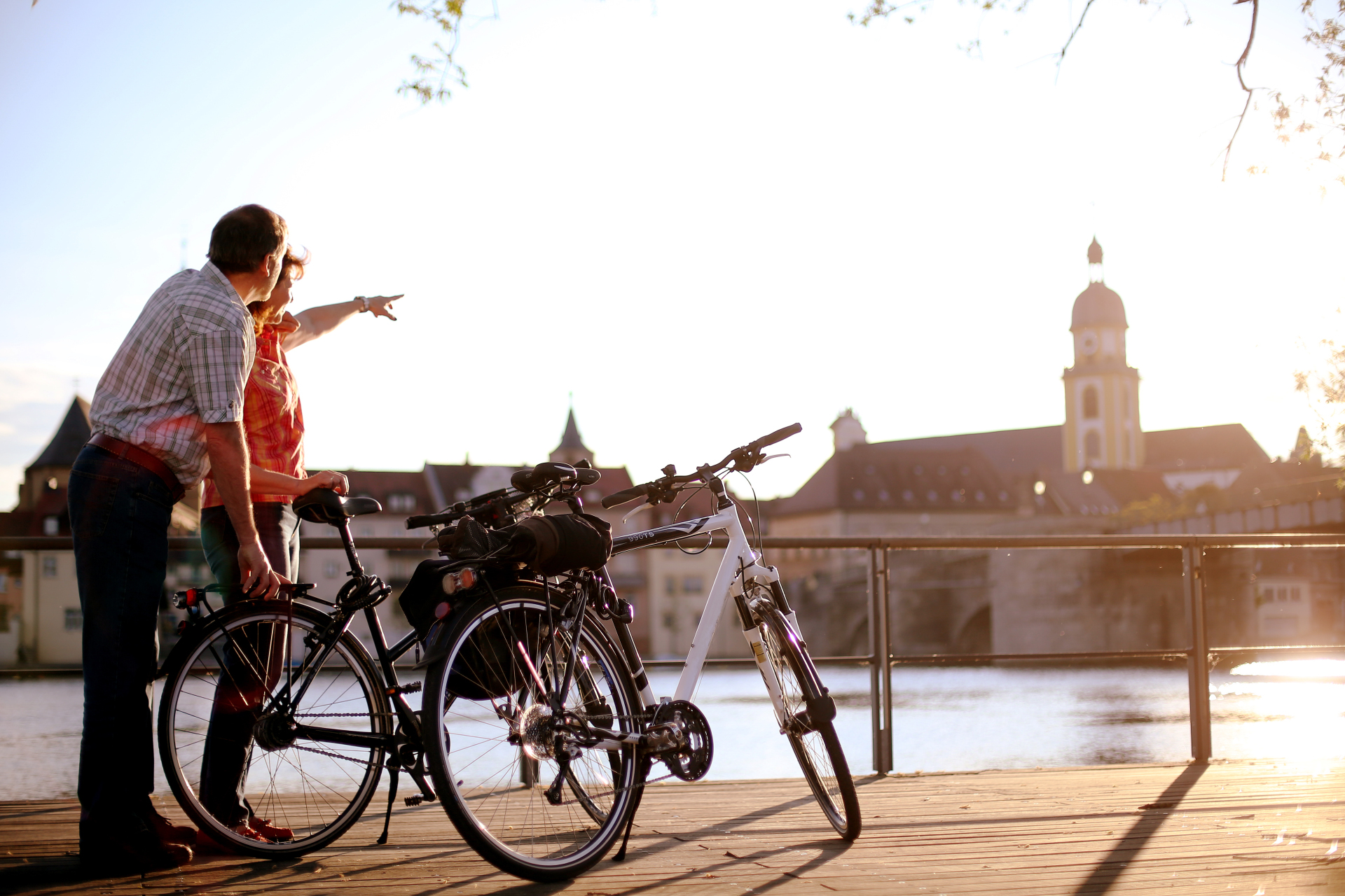 A couple are standing with their bicycles on the city balcony. The woman points to the Protestant town church on the other side of the Main.