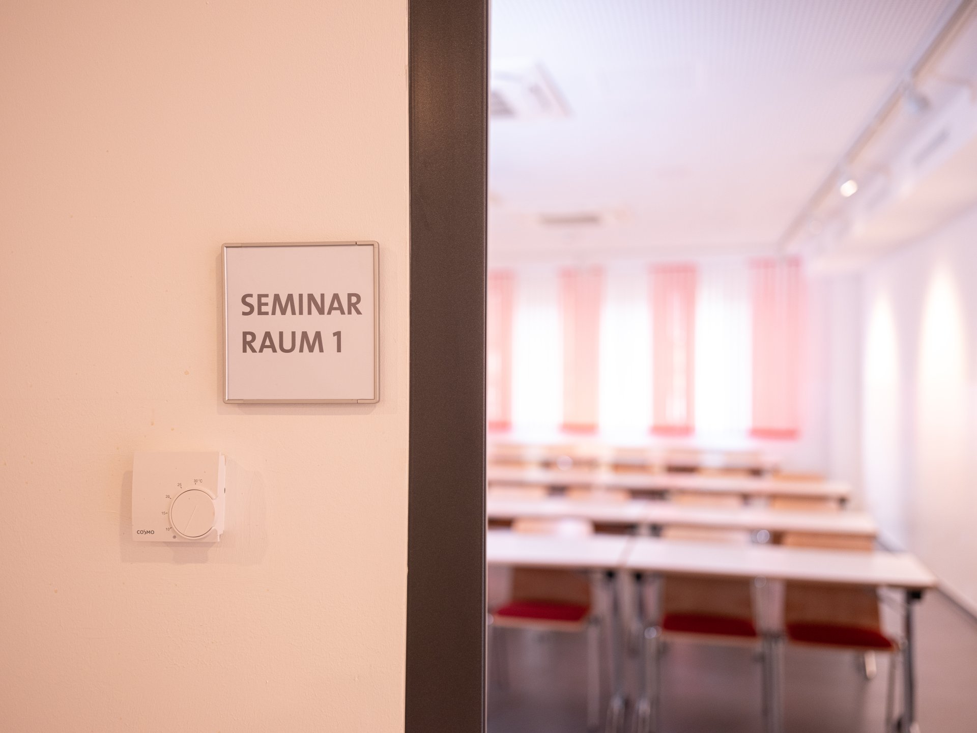 Open door with a view of tables and chairs standing in a row. There is a sign on the wall next to the door. It says "Seminar room 1"