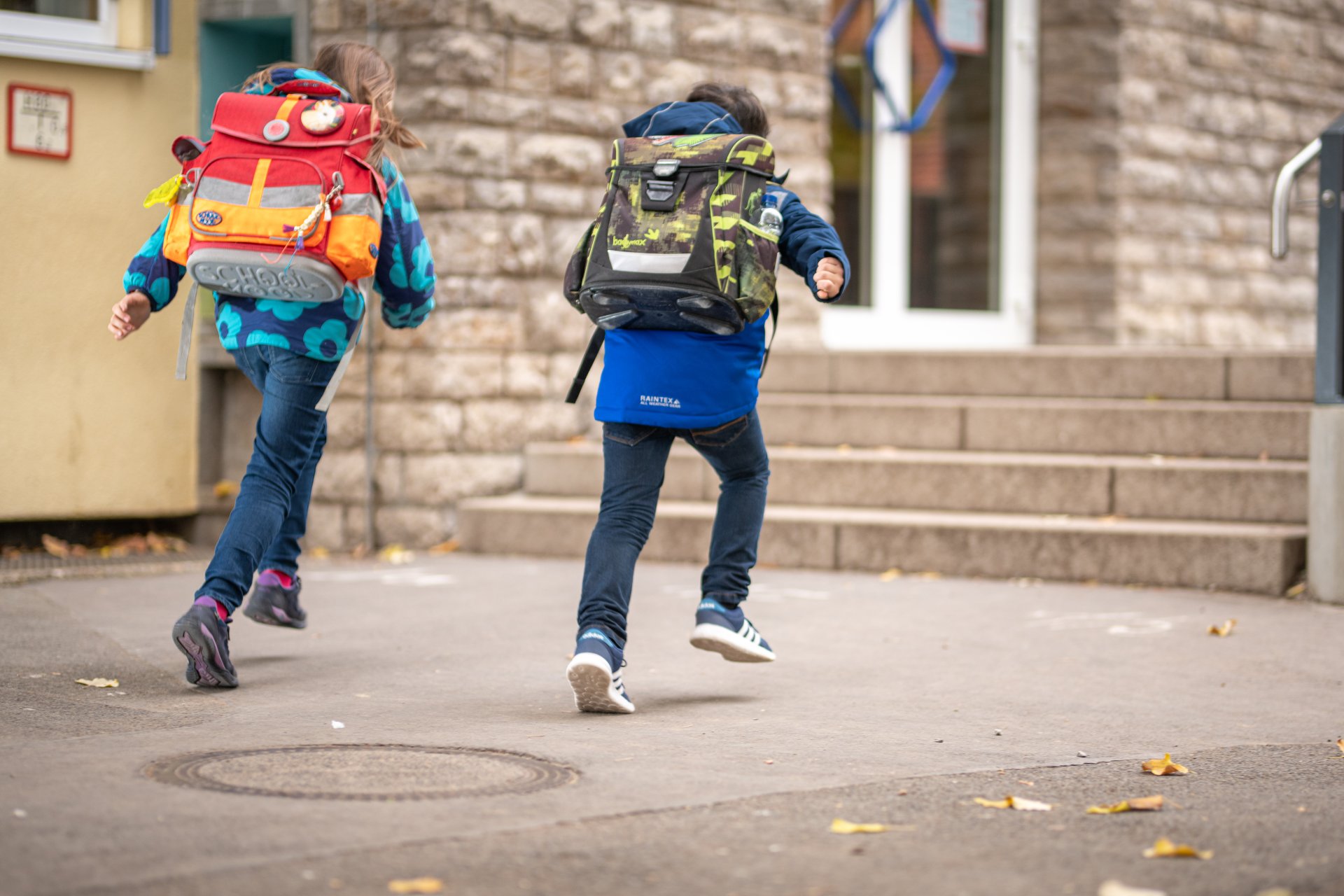 Grundschüler auf dem Pausenhof Zwei Grundschüler laufen mit ihren Schulranzen auf den Eingang der Schule zu.