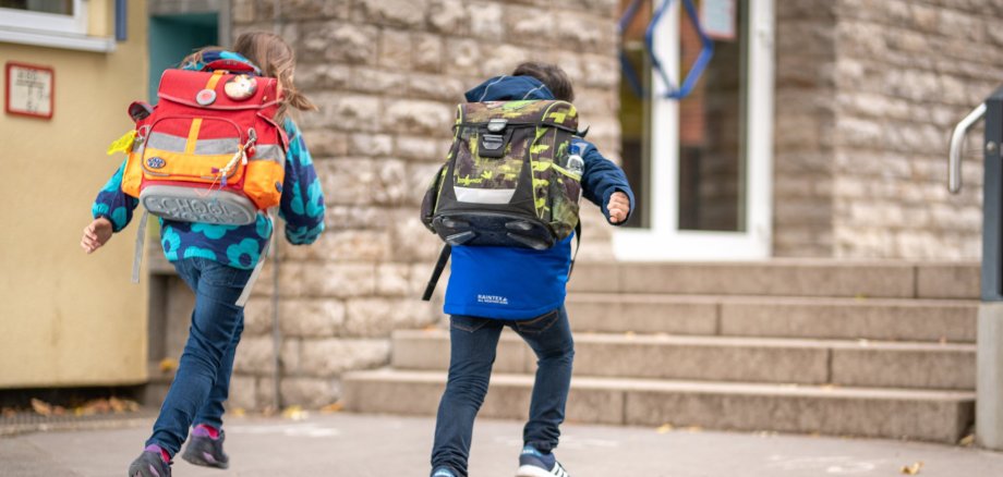Grundschüler auf dem Pausenhof Zwei Grundschüler laufen mit ihren Schulranzen auf den Eingang der Schule zu.