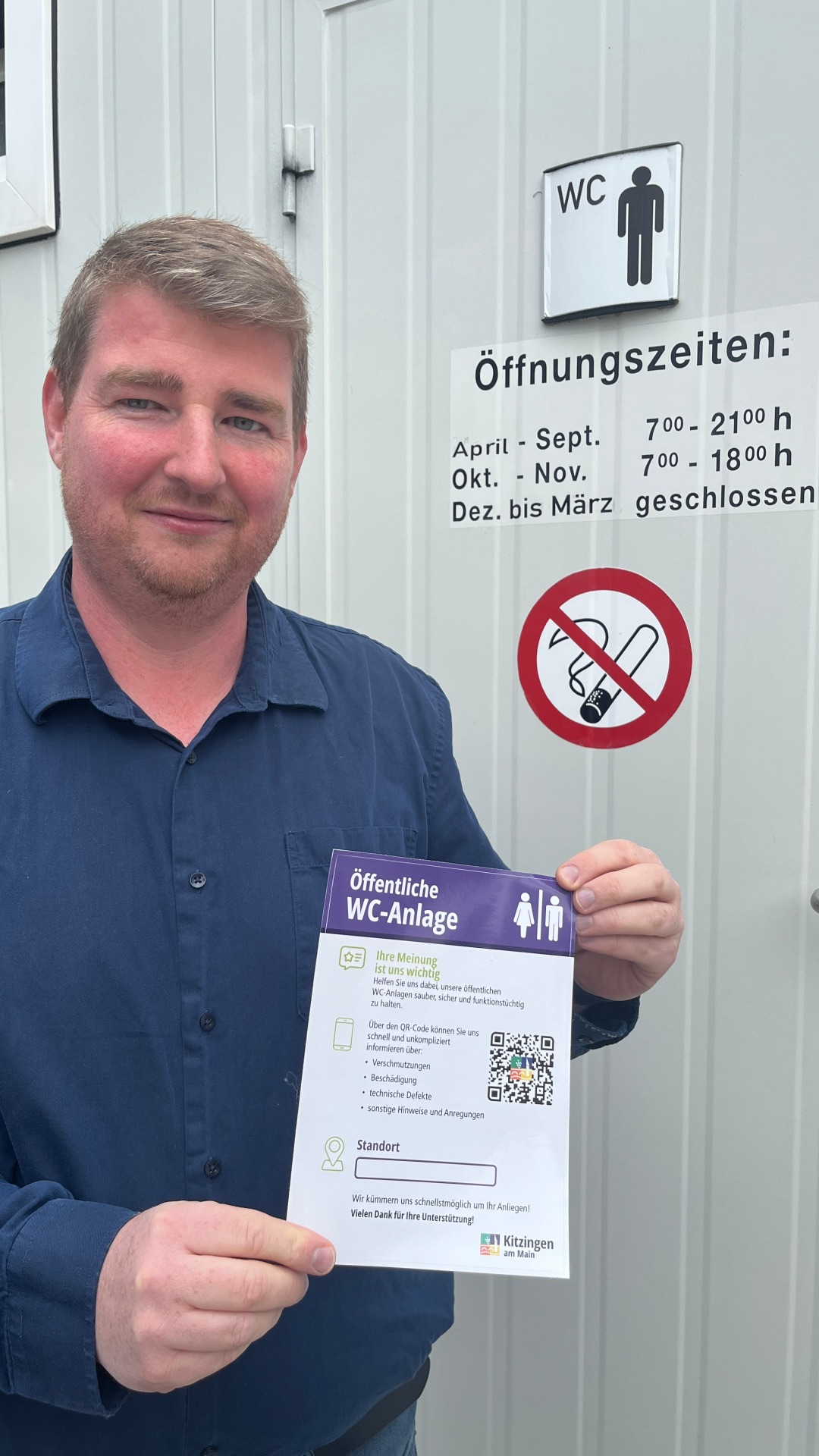 Patrick Fischer, Leiter des Zentralen Gebäudemanagements der Stadt, hält den Hinweis mit dem QR-Code in die Kamera. Nutzer der öffentlichen WC-Anlagen können Verschmutzungen oder Schäden ab sofort unbürokratisch und schnell melden.   