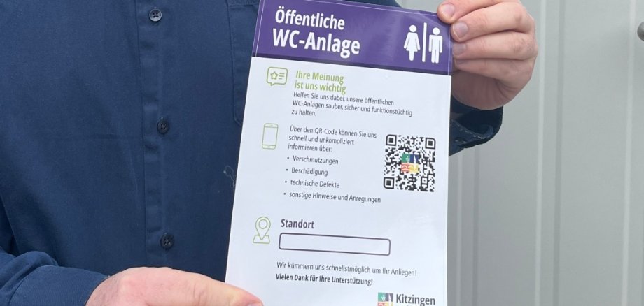 Patrick Fischer, Leiter des Zentralen Gebäudemanagements der Stadt, hält den Hinweis mit dem QR-Code in die Kamera. Nutzer der öffentlichen WC-Anlagen können Verschmutzungen oder Schäden ab sofort unbürokratisch und schnell melden.   