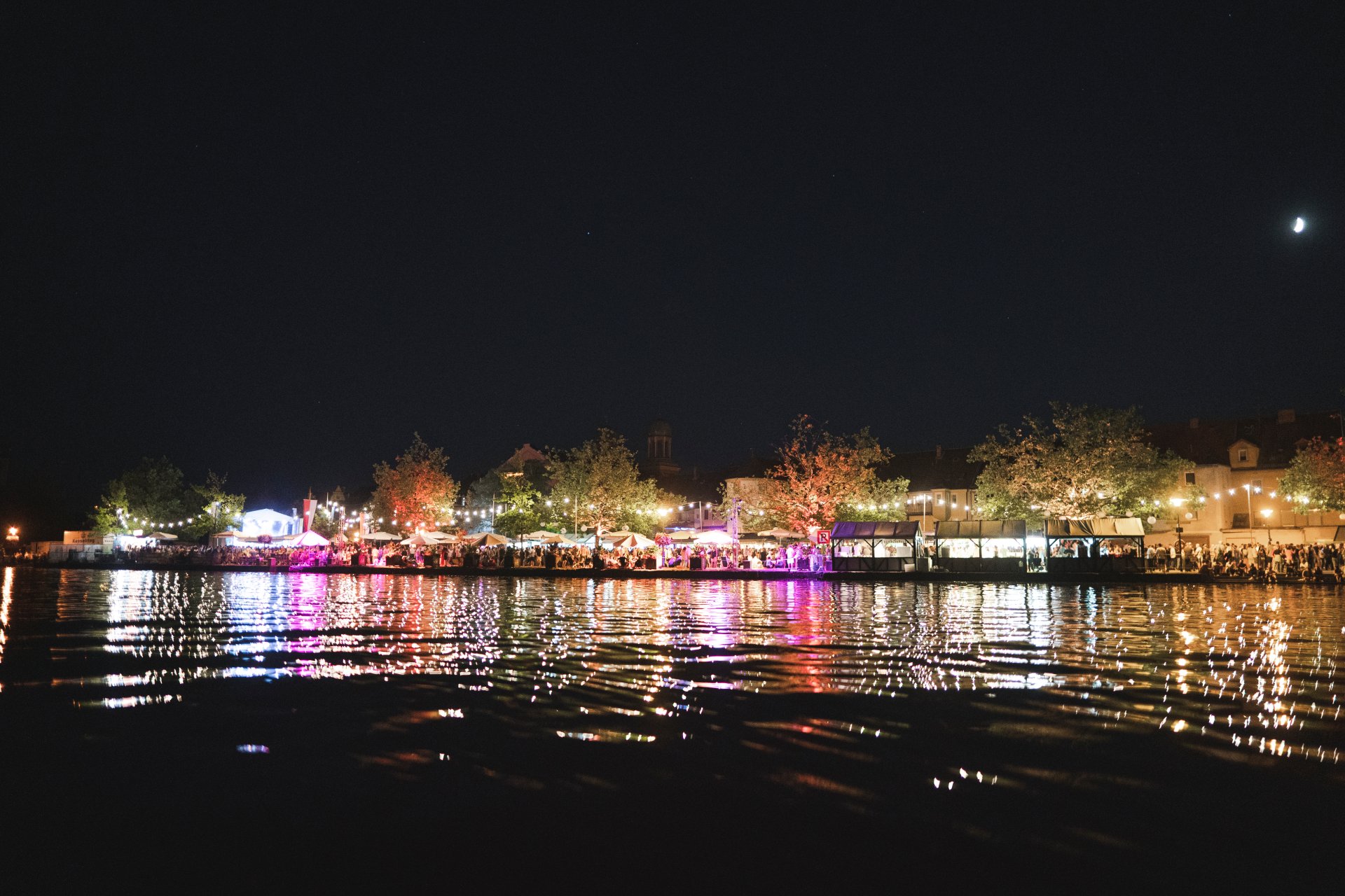 Blick auf die bunt schillernde Uferpromenade während des Weinfestes bei Nacht.