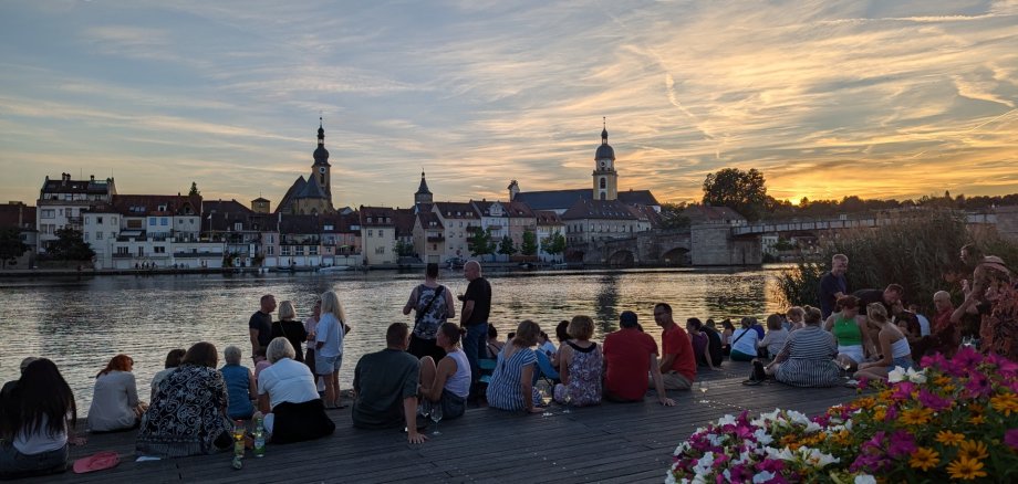 Leute am Stadtbalkon an einem Abend, im Hintergrund die Stadtsilhouette