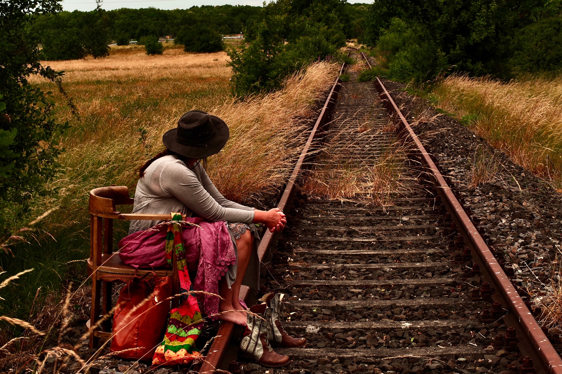 Eine Frau sitzt an verlassenen Schienen.